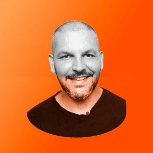 Um homem com barba sorrindo diante de um fundo laranja.