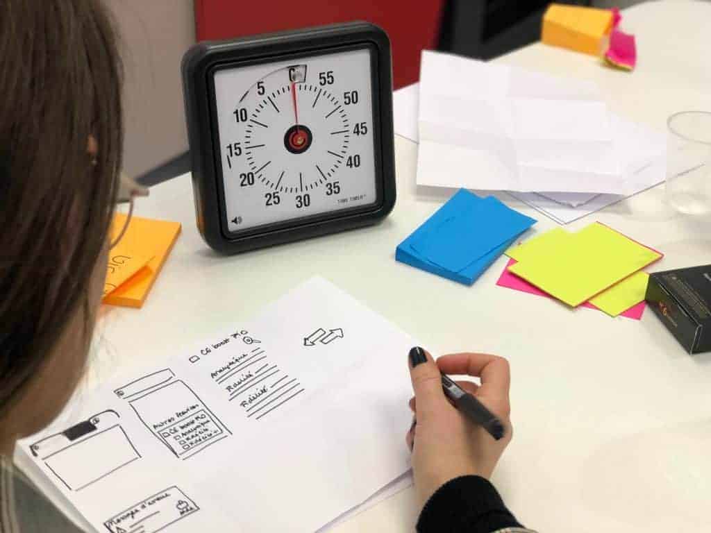 Uma mulher debatendo ideias em uma mesa com um relógio e post-its durante um curso de criatividade.