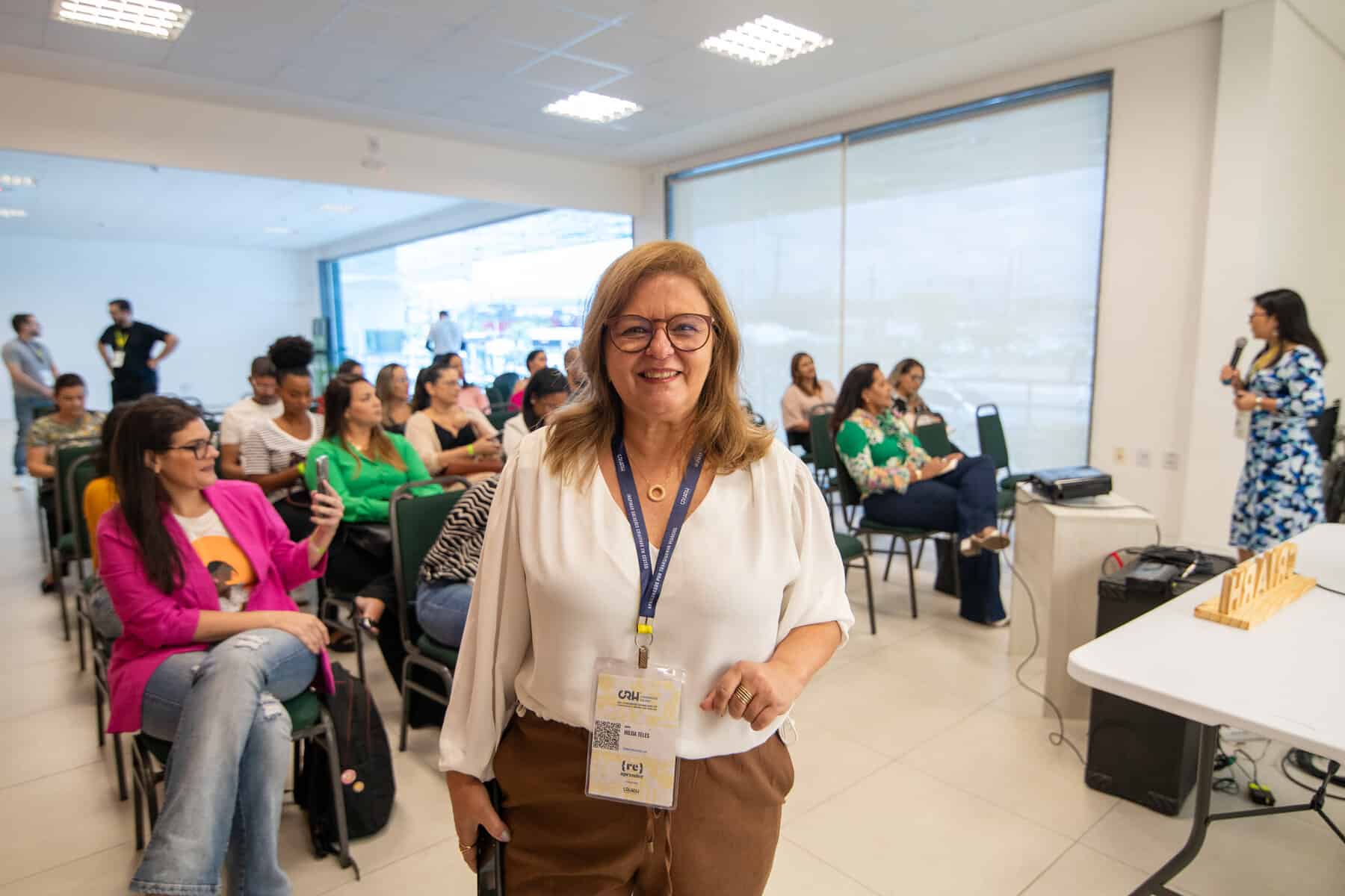 Uma mulher parada em frente a uma sala cheia de gente.