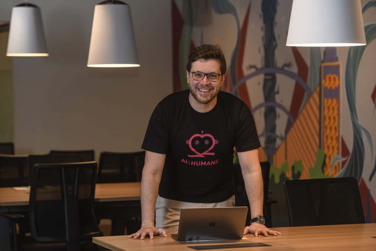 Um homem sorridente, de óculos e camiseta preta com a inscrição 